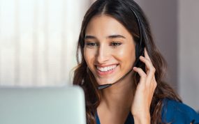 Smiling woman using laptop while talking to customer on phone. Consulting corporate client in conversation with customer using computer on desk. Service desk consultant talking in a call center and working on laptop.