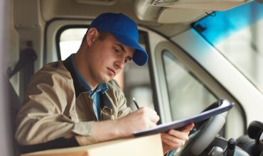 Young courier filling the form while sitting in the car he delivering the package