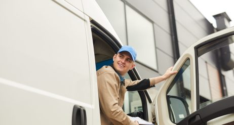 Young smiling courier holding package while sitting in the van he delivering parcels