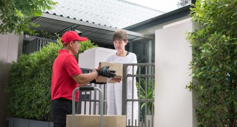 Asian delivery man in red uniform delivering parcel boxes to woman recipient at home